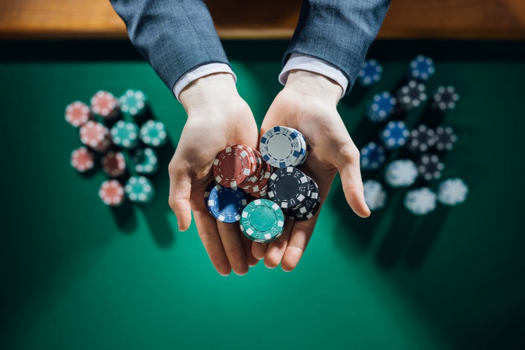 elegant male casino player holding a handful of chips with green table on background, hands close up top view